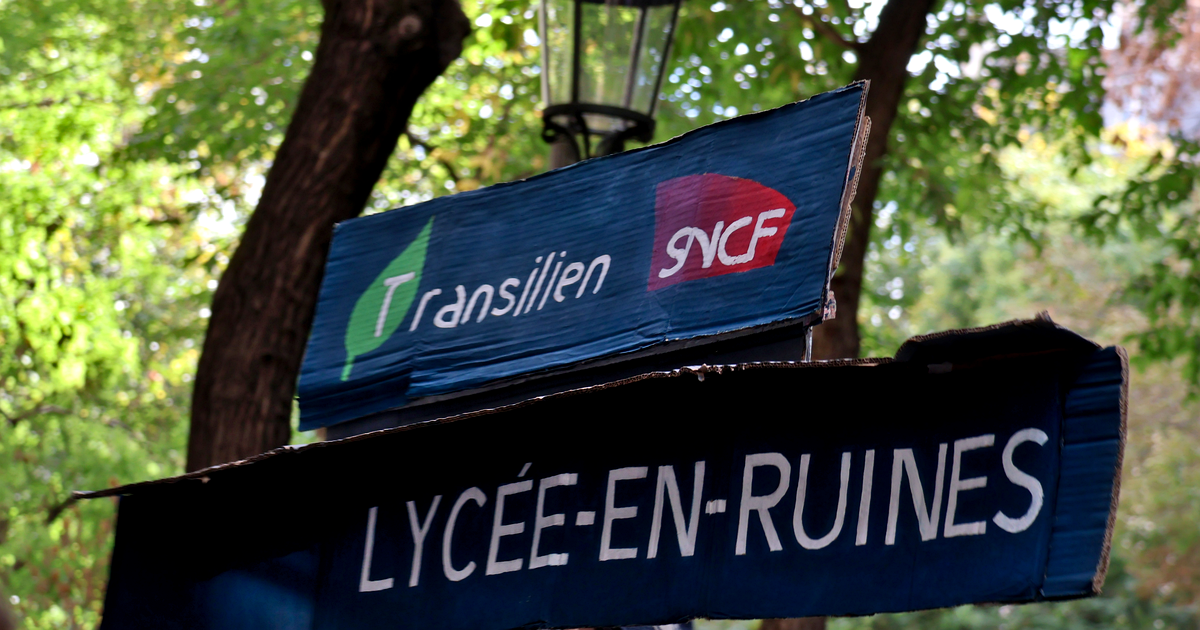 Hand-painted blue cardboard placard reading LYCÉE-EN-RUINES with Transilien and SNCF logos, held up at a Paris protest among trees.