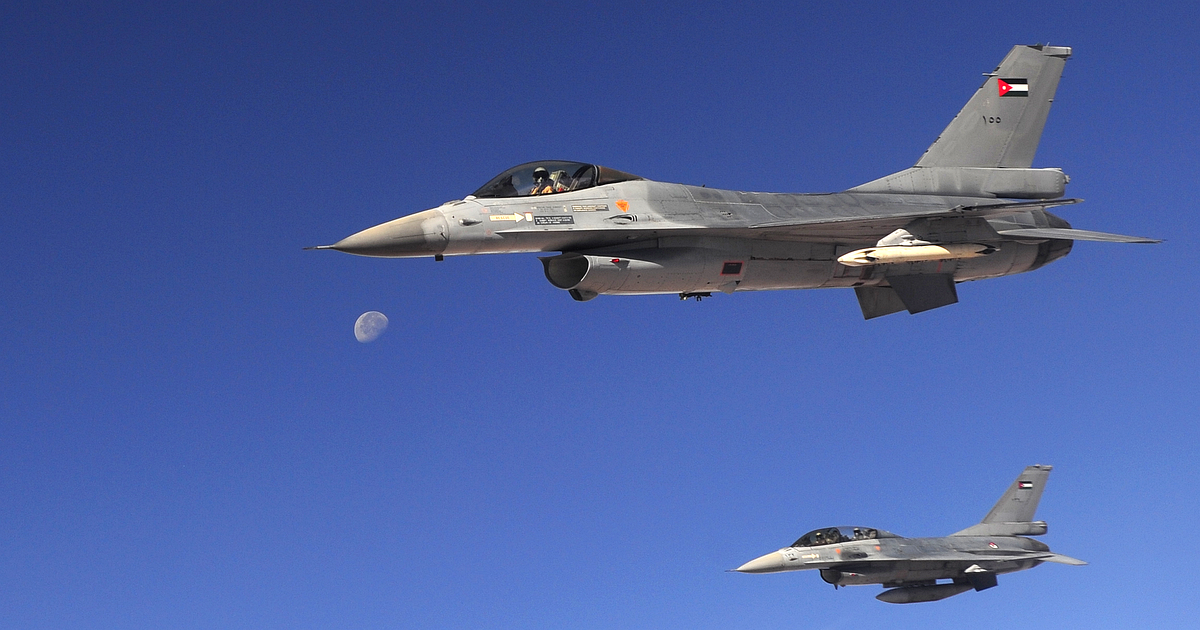 Two Royal Jordanian Air Force F-16 fighter jets, Jordanian flags on their tails, fly in formation against a deep blue sky with the moon visible.