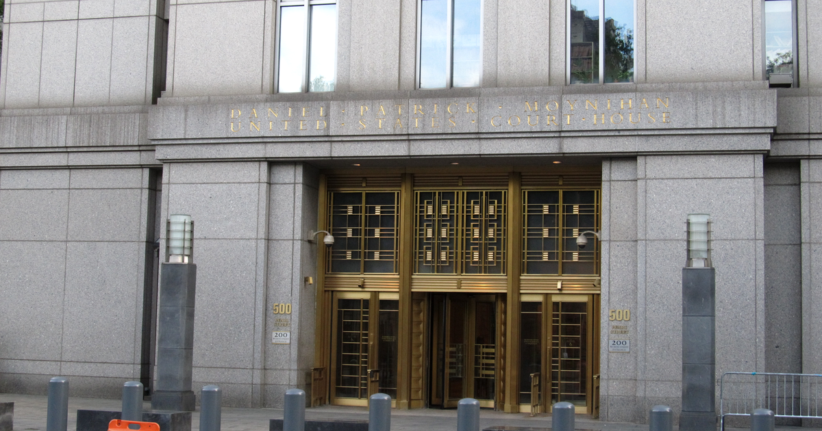 The granite entrance of a federal courthouse: gold lettering reading Daniel Patrick Moynihan United States Court House above bronze-framed glass doors, the number 500 beside them and steel bollards along the sidewalk.