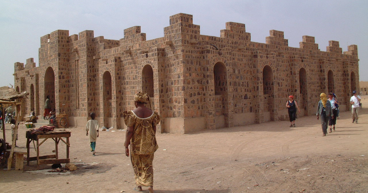 Crenellated stone-block building, the Maison des artisans, on a sandy street in Kidal, northern Mali, with a few passers-by, January 2005.