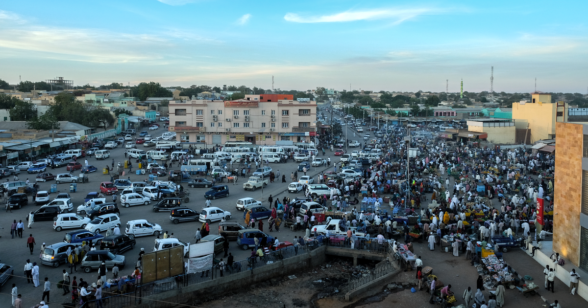 A crowded market square and main road in central el-Fasher, full of cars and people, in December 2017, before the war