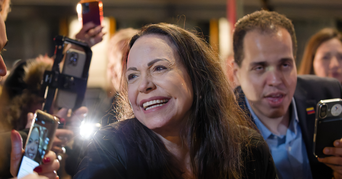 María Corina Machado smiles as supporters hold up phones to photograph her outside a hotel in Oslo at night.